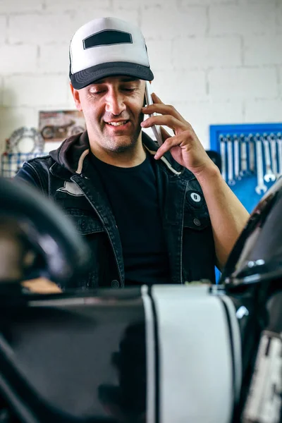 Mechanic talking phone while fixing motorbike — Stock Photo, Image