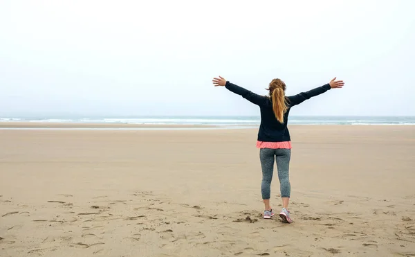 Mujer joven mirando el mar con las manos en alto — Foto de Stock