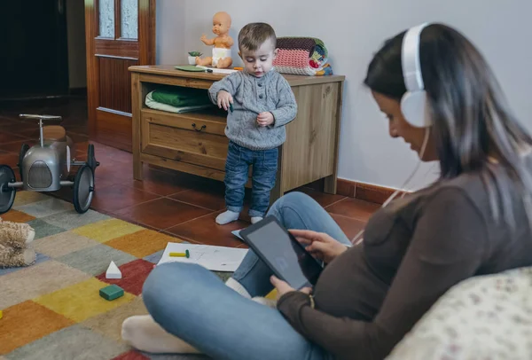 Pregnant using the tablet while her son is playing — Stock Photo, Image