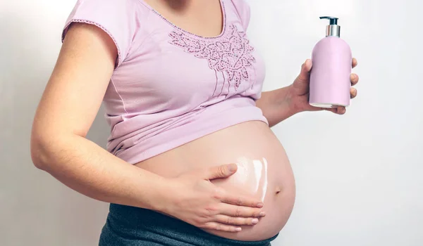 Schwangere cremen sich mit Dehnungsstreifen ein — Stockfoto