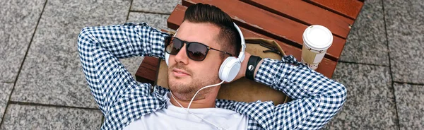 Mannen med hörlurar liggande på en bänk — Stockfoto