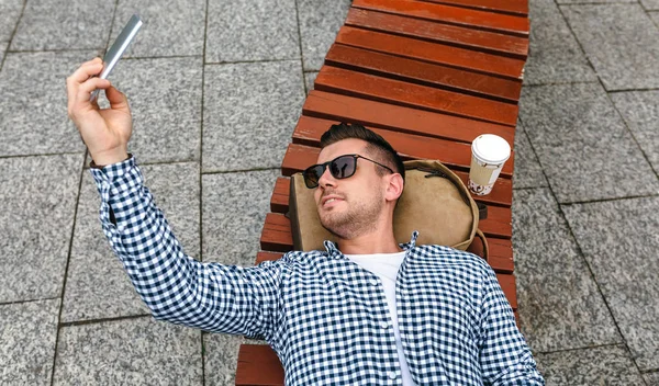 Muž leží na lavičce v parku takže selfie s mobile — Stock fotografie