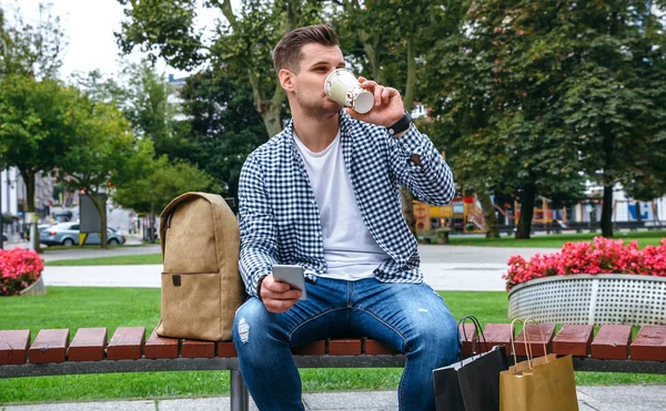 Uomo con mobile bere caffè seduto su una panchina — Foto Stock