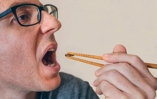 Man in profile eating a cricket with chopsticks