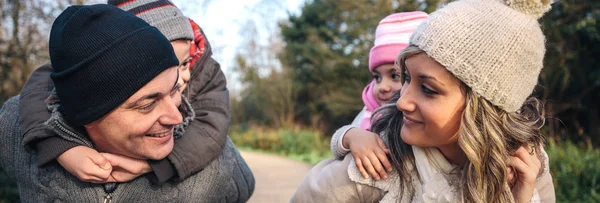 Parents giving piggyback ride to happy children outdoors — Stock Photo, Image