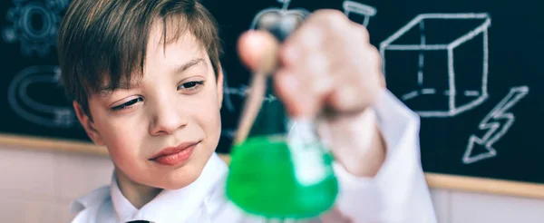 Serious boy looking flask with chemical liquid