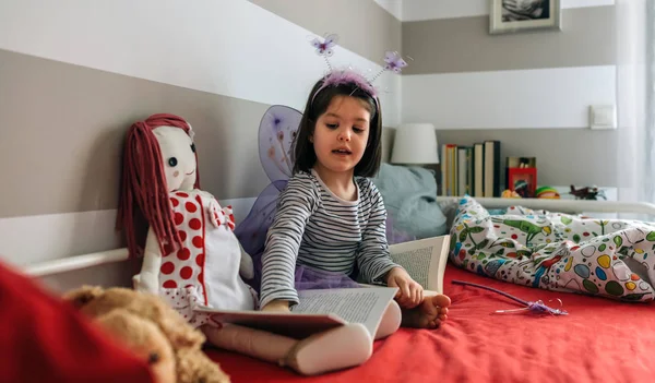 Meisje vermomd als een dagvlinder onderwijs haar pop te lezen — Stockfoto