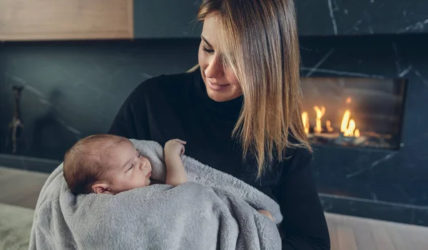 Moeder haar baby bij open haard knuffelen — Stockfoto