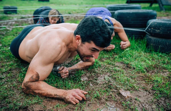 Male participant in an obstacle course crawling — Stock Photo, Image
