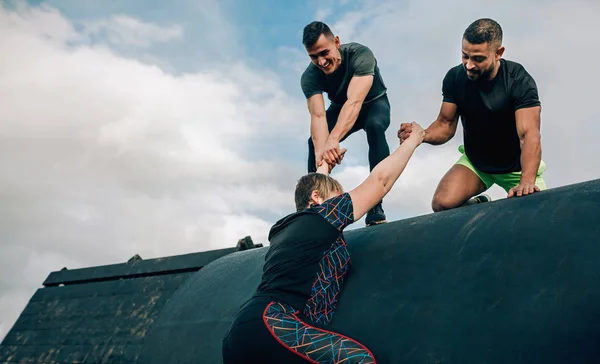 Woman in an obstacle course climbing a drum with teammates — Stock Photo, Image