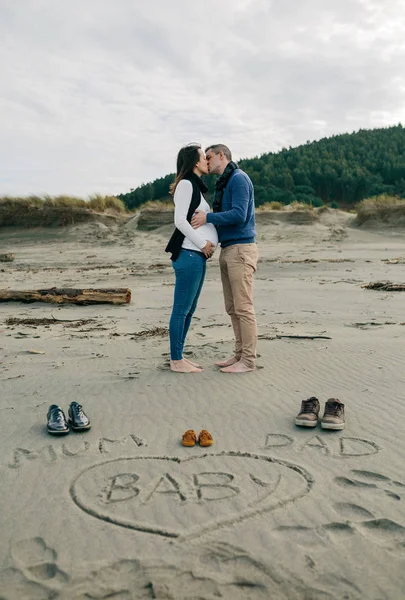 Mama, Papa und Baby auf den Sand geschrieben, während sich die Eltern dahinter küssen — Stockfoto