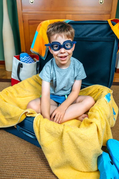 Chico divertido sonriendo sentado dentro de una maleta — Foto de Stock