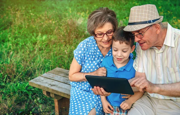 Бабушка с дедушкой и внук сидят на скамейке на планшете — стоковое фото