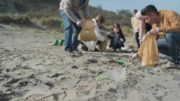 Plastic bekers en rietjes op het strand en de groep van vrijwilligers schoonmaken — Stockvideo