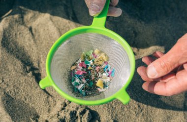Colander with microplastics on the beach clipart