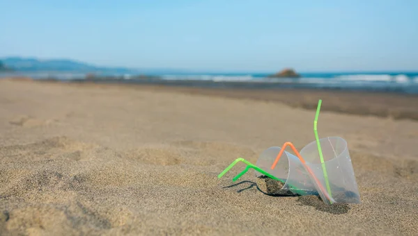 Praia com copos de plástico e palhas — Fotografia de Stock