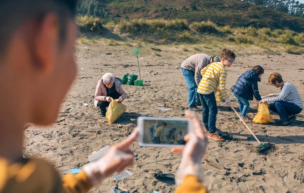 Jongeman maakt foto naar groep vrijwilligers schoonmaken strand — Stockfoto