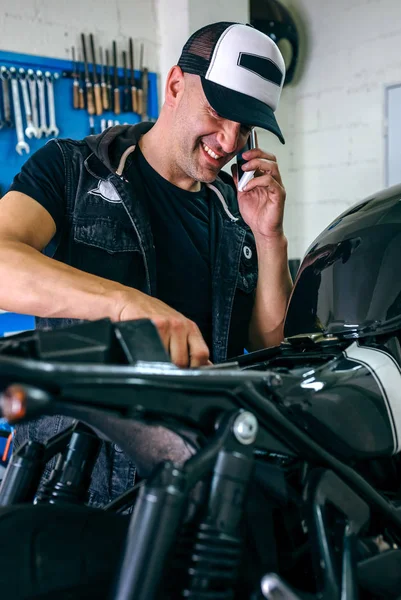 Mechanic talking phone while fixing motorbike — Stock Photo, Image