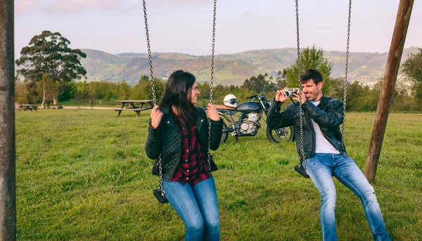 Young man taking a picture of his girlfriend on the swings — Stock Photo, Image