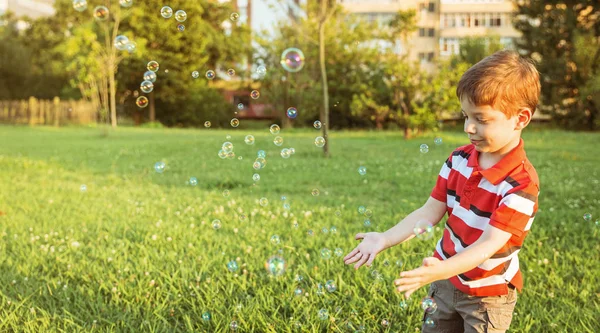 Happy boy playing with soap bubbles in the park — Stock Photo, Image