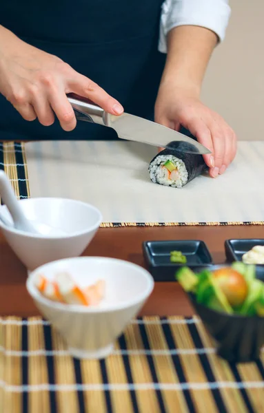 Vrouwelijke chef-kok snijden Japanse sushi roll — Stockfoto