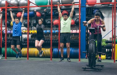 Spor salonunda barfiks çeken ve bisiklet kullanan sporcular