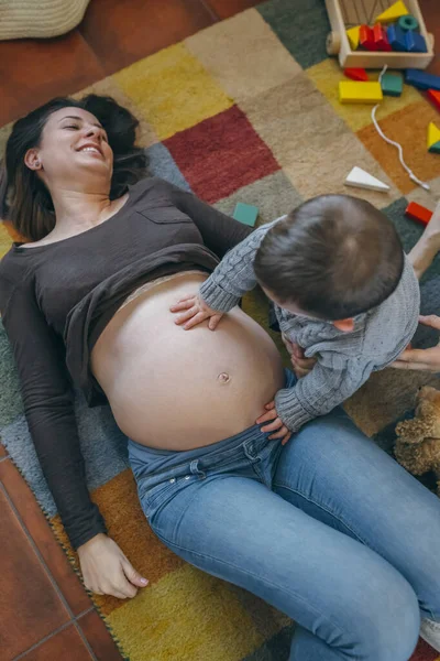 Тоддлер ласкает живот беременной матери. — стоковое фото