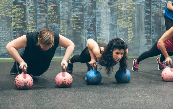 Sportswomen doing push-ups with kettlebells — Stock Photo, Image