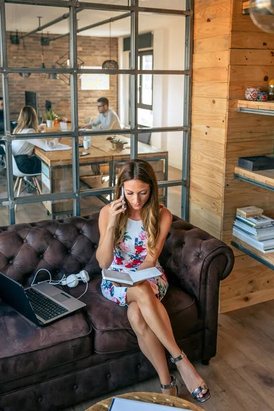 Businesswoman working with laptop talking on the phone sitting on the sofa — Stock Photo, Image