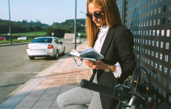 Businesswoman lecture journal avec son scooter prochaine — Photo