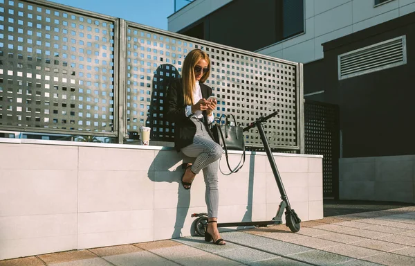 Bizneswoman za pomocą telefonu komórkowego ze swoim skuterem obok — Zdjęcie stockowe