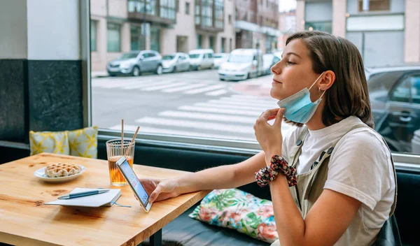 Woman taking off protective mask in a cafe — Stock Photo, Image