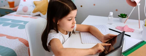 Chica estudiando en casa con la tableta y la máscara en la mesa —  Fotos de Stock