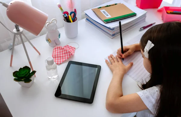 Ragazza che studia a casa con tablet e maschera sul tavolo — Foto Stock