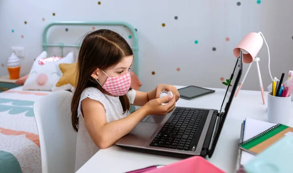 Chica aplicando desinfectante de manos mientras estudia con el ordenador portátil — Foto de Stock