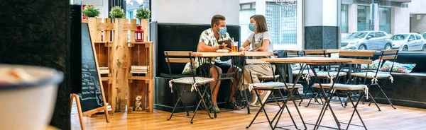 Пара в маске для лица, пьющие в кафе — стоковое фото