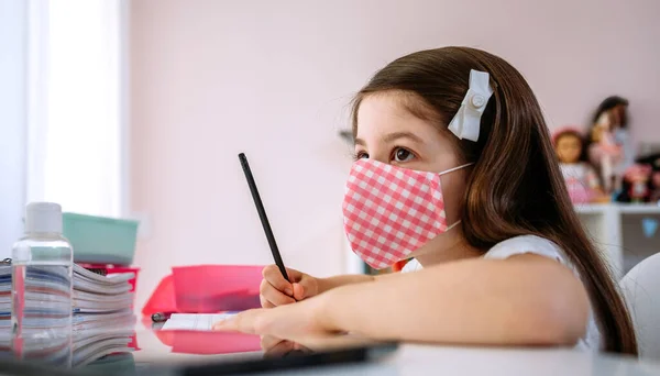 Chica con máscara haciendo la tarea en su dormitorio — Foto de Stock
