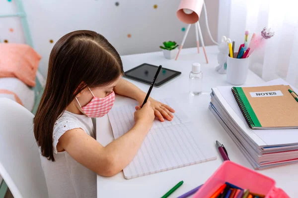 Chica con máscara haciendo la tarea en su dormitorio — Foto de Stock