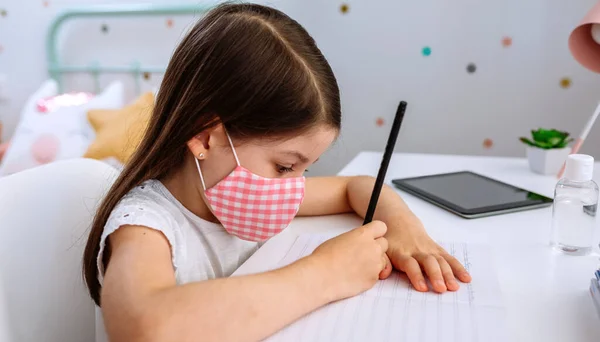 Chica con máscara haciendo la tarea en su dormitorio — Foto de Stock