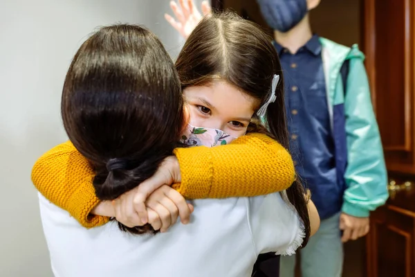 Madre abrazando a hija con máscara volviendo de la escuela —  Fotos de Stock