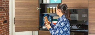 Acil durum kilerine su, konserve yiyecek ve ilk yardım çantası da dahil olmak üzere kurabiye paketleri ekleyen kadın pankartı. Kadın 72 saat boyunca doğal afet ve elektrik kesintisi için hayatta kalma kiti hazırlıyor.