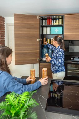 Anne ve kız, 72 saatlik acil durum çantasına kurabiye paketleri ekliyor. Savaş ya da yiyecek sıkıntısına karşı hazırlar. Aile, mutfakta acil durum kileri hazırlamak için işbirliği yapıyor.