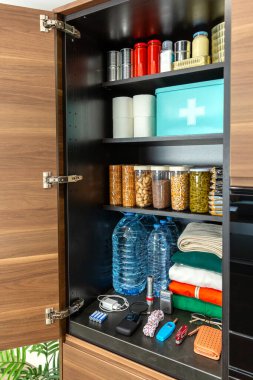 Potansiyel acil durumlar ya da yiyecek kıtlığı için depolanmış bir dolap. 72 saat hayatta kalma çantası konsepti. Yiyecek ve içecek malzemeleri, konserve yiyecekler, bozulamayan eşyalar ve giysilerle organize edilmiş modern mutfak kileri.