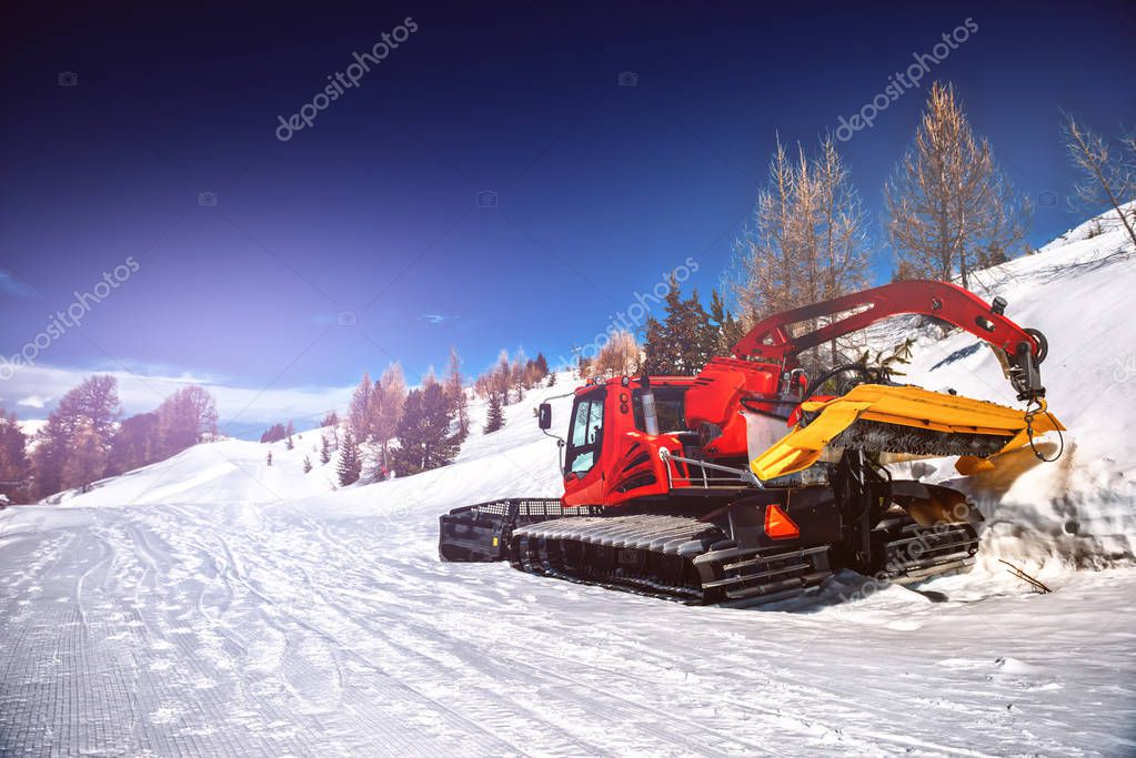 Winter landscape with snow plowing bulldozer. Snow removal equipment for a ski resort. Mountains background