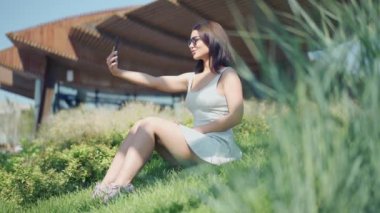 Genç kadın yeşil çimenlerin üzerinde oturan selfie yapma