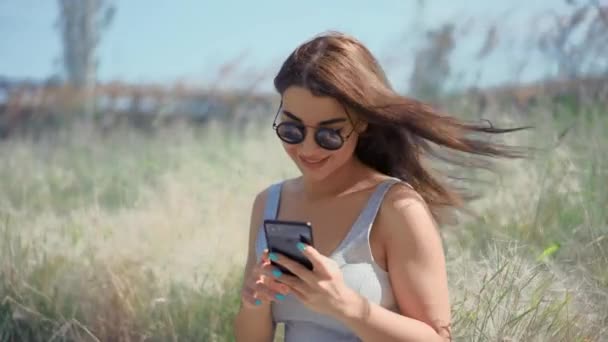 Junge Frau chattet mit Freunden per Smartphone im sonnigen Park. — Stockvideo