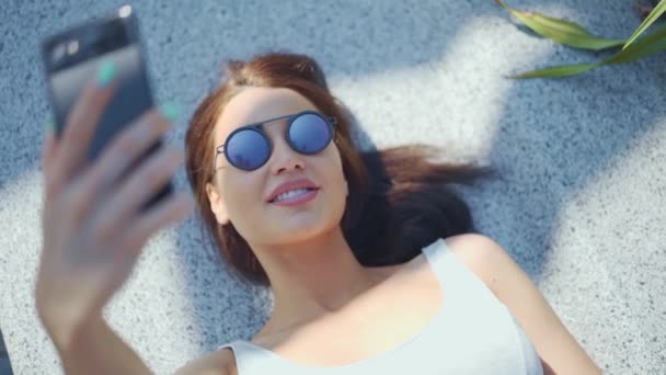 Attractive young girl making selfie and lying in the park — Stock Video