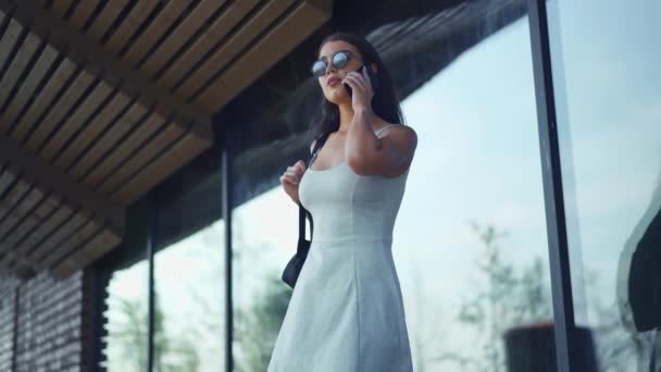 Ung kvinna pratar i telefonen på bakgrund av blanka dörrar — Stockvideo