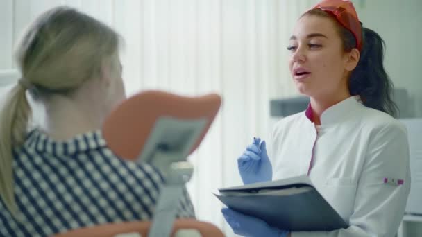 Vrouwelijk tandarts met Klembord en patiënt vrouw op kantoor van de tandheelkundige kliniek — Stockvideo