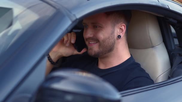 Улыбающийся молодой человек звонит по смартфону во время вождения автомобиля — стоковое видео